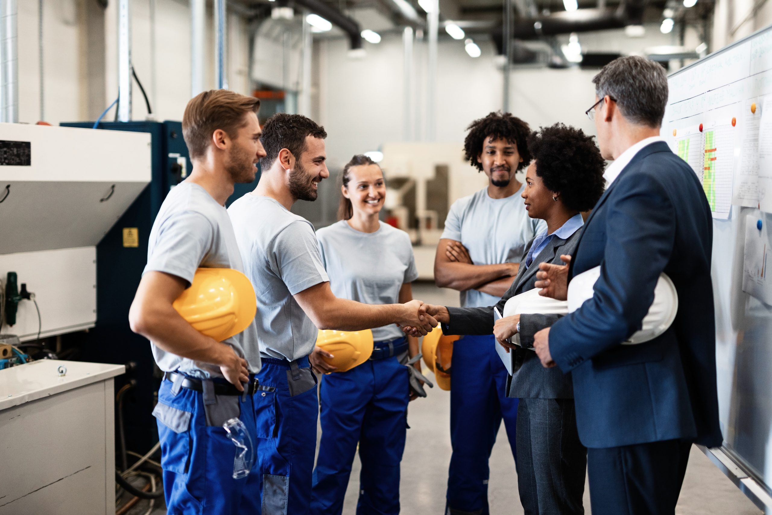 Company managers visiting their employees in a factory. Happy African American businesswoman is shaking hands with one worker.